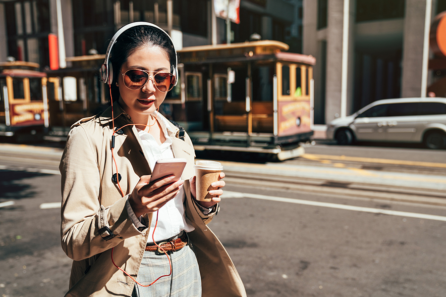 Client Center - Woman Walking Through San Francisco, Past Cable Cars, Wearing Headphones and Sunglasses and Uses Her Phone